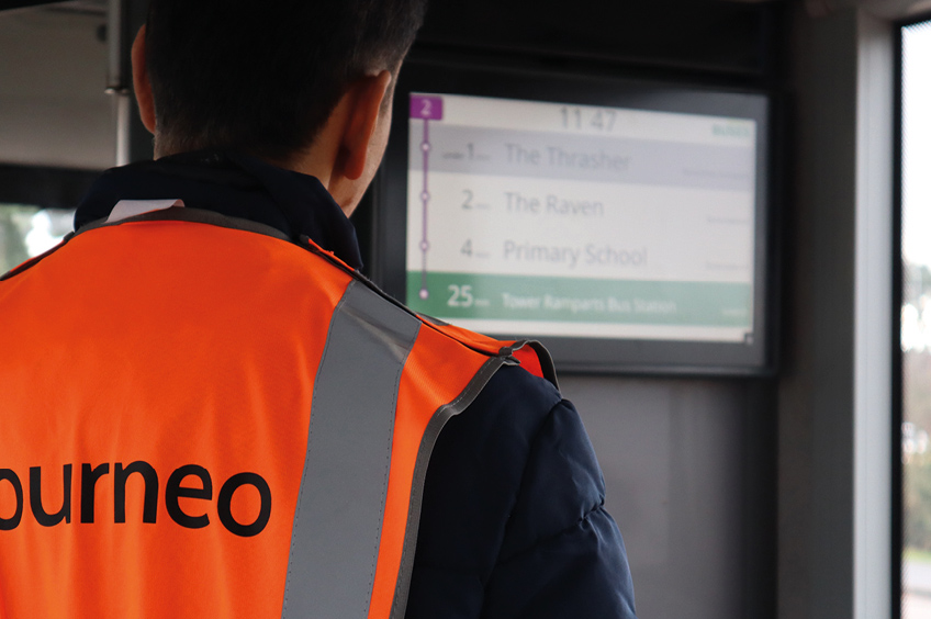 The image shows a Journeo engineer configuring or repairing a PSVAIR-compliant display on a bus.