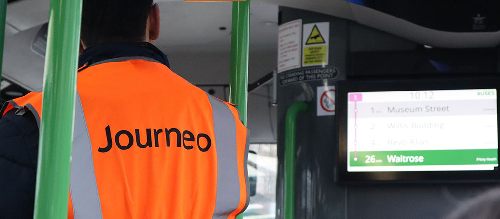The image shows a Journeo engineer on a bus commissioning a PSVAIR-complaint display.